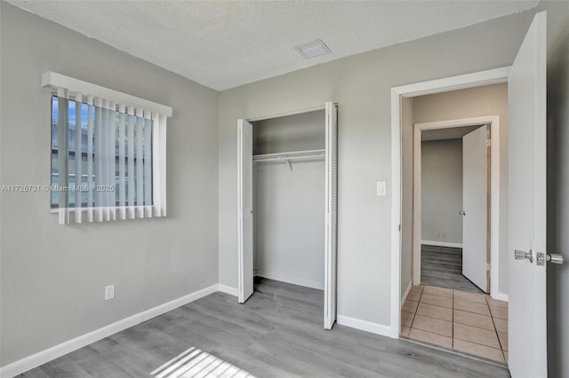 unfurnished bedroom with a textured ceiling, a closet, and light hardwood / wood-style flooring