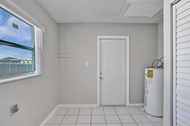 laundry room featuring water heater, light tile patterned floors, and a textured ceiling