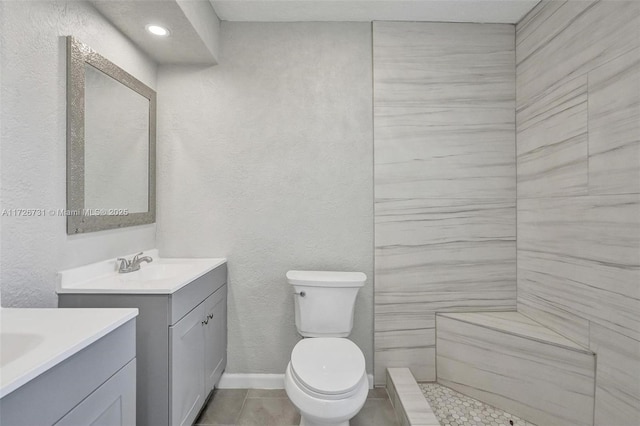 bathroom featuring toilet, vanity, tile patterned floors, and a tile shower