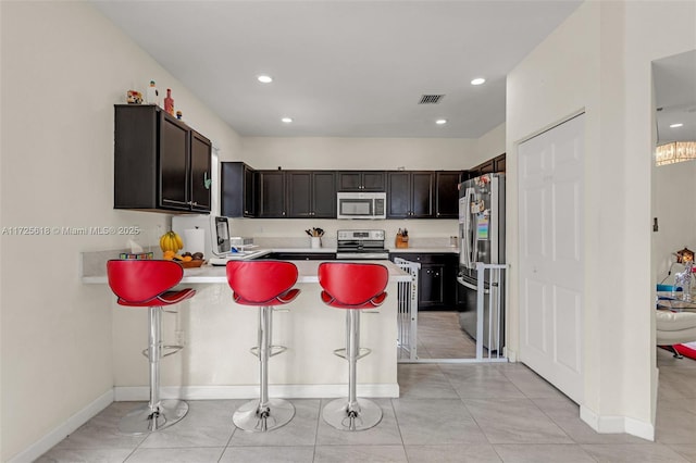 kitchen with dark brown cabinetry, stainless steel appliances, a kitchen breakfast bar, kitchen peninsula, and light tile patterned flooring