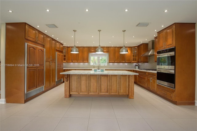 kitchen featuring light stone counters, hanging light fixtures, a center island, and wall chimney exhaust hood