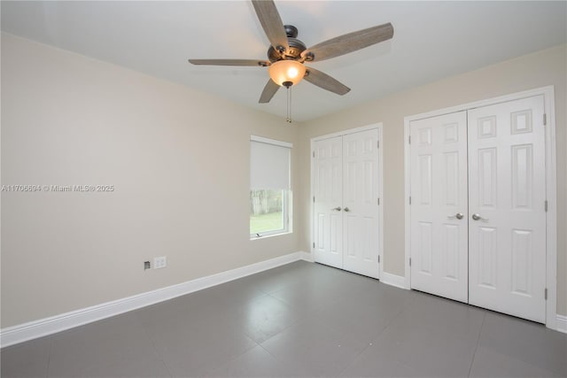 unfurnished bedroom with multiple closets, tile patterned flooring, baseboards, and a ceiling fan