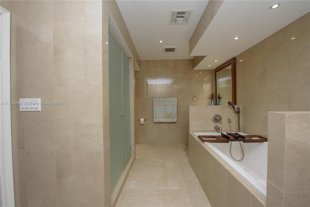 bathroom with vanity, tile walls, and a relaxing tiled tub