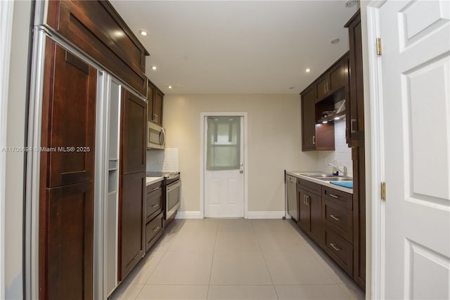 kitchen featuring light tile patterned flooring, dark brown cabinetry, stainless steel appliances, a sink, and decorative backsplash