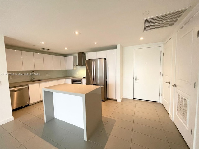 kitchen with white cabinets, appliances with stainless steel finishes, wall chimney exhaust hood, a kitchen island, and sink