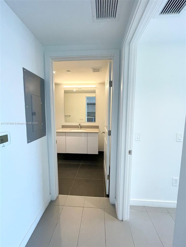 hall featuring light tile patterned floors, electric panel, and sink