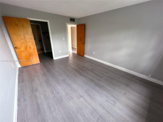 unfurnished bedroom with dark wood-style floors, a walk in closet, visible vents, and baseboards