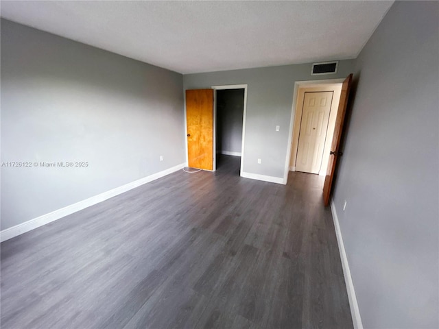 unfurnished bedroom with a textured ceiling, dark wood-style flooring, visible vents, baseboards, and a closet