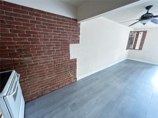 unfurnished room featuring brick wall, baseboards, ceiling fan, and dark wood-type flooring