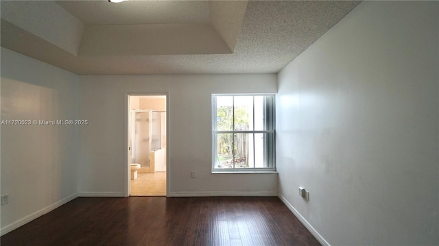 unfurnished room featuring a textured ceiling, dark wood-type flooring, and a tray ceiling