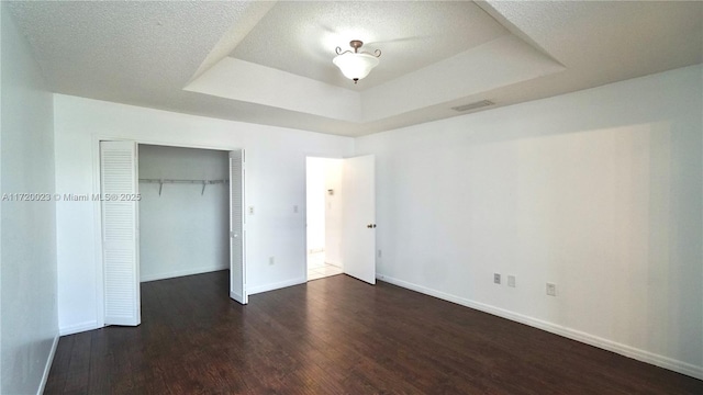 unfurnished bedroom with a textured ceiling, a closet, dark hardwood / wood-style floors, and a tray ceiling