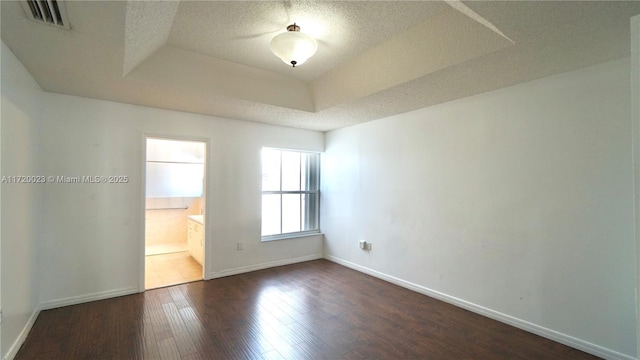 spare room with a raised ceiling, dark wood-type flooring, and a textured ceiling