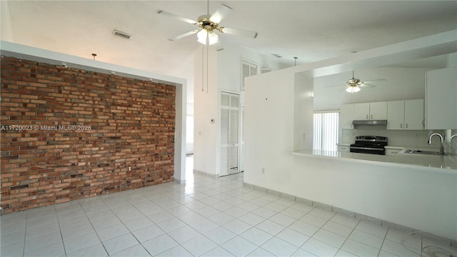 kitchen with sink, light tile patterned flooring, white cabinets, black / electric stove, and brick wall