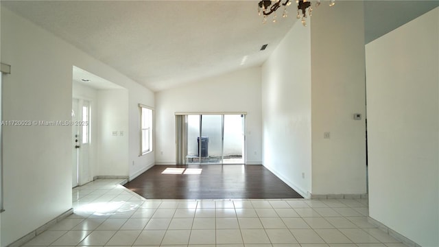 tiled empty room featuring vaulted ceiling and a chandelier