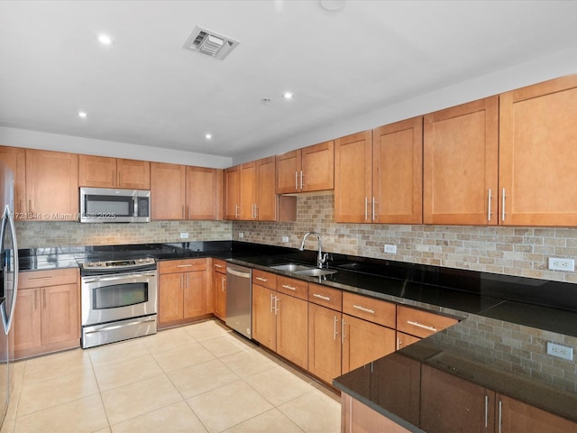 kitchen with appliances with stainless steel finishes, dark stone counters, tasteful backsplash, sink, and light tile patterned floors