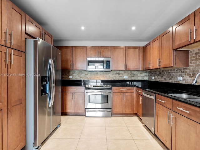 kitchen with appliances with stainless steel finishes, tasteful backsplash, light tile patterned flooring, dark stone countertops, and sink