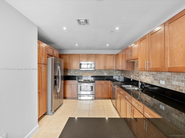 kitchen with light tile patterned floors, appliances with stainless steel finishes, tasteful backsplash, dark stone countertops, and sink