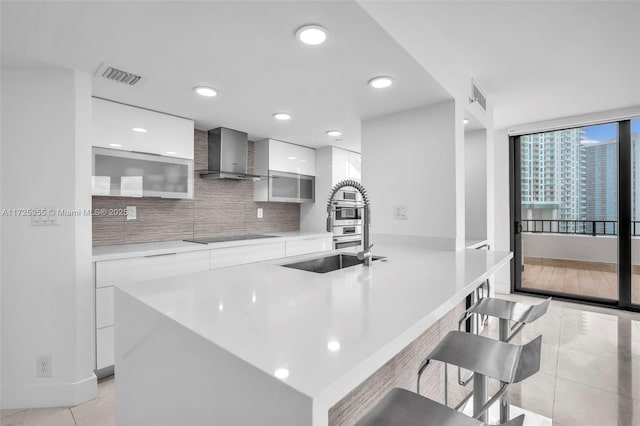 kitchen with a kitchen bar, white cabinetry, wall chimney range hood, tasteful backsplash, and light tile patterned floors