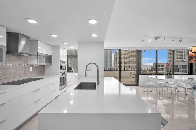 kitchen featuring black electric stovetop, wall chimney range hood, a spacious island, and sink