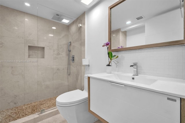 bathroom featuring backsplash, toilet, vanity, and a tile shower