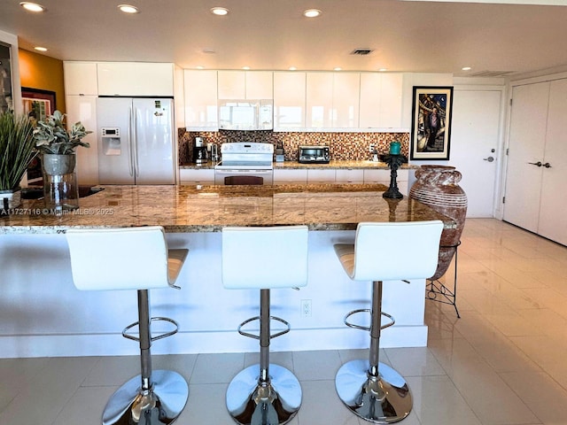 kitchen with light tile patterned floors, white cabinets, a breakfast bar, and white appliances