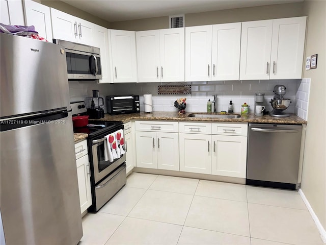 kitchen featuring stainless steel appliances, white cabinets, dark stone counters, and sink