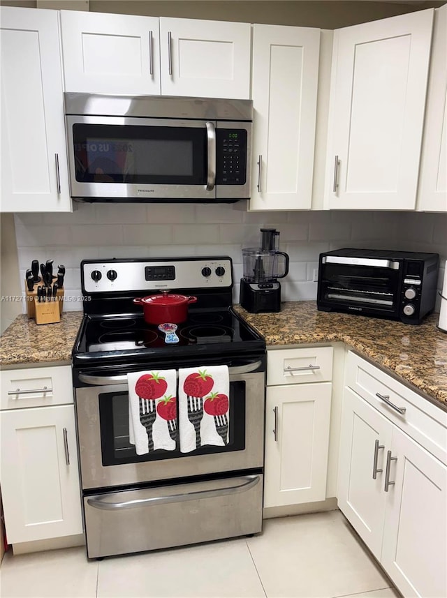 kitchen featuring white cabinetry, stainless steel appliances, and dark stone counters