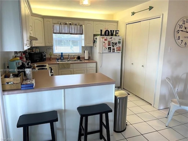 kitchen featuring white fridge, kitchen peninsula, light tile patterned flooring, range hood, and sink