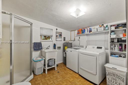 washroom with water heater, washing machine and clothes dryer, light parquet flooring, a textured ceiling, and sink