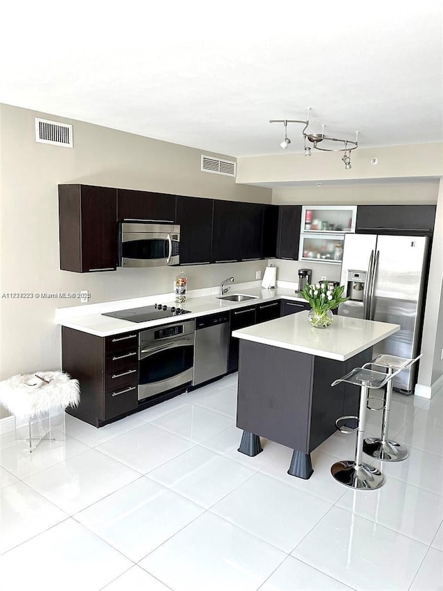 kitchen featuring a center island, a kitchen bar, sink, stainless steel appliances, and light tile patterned floors