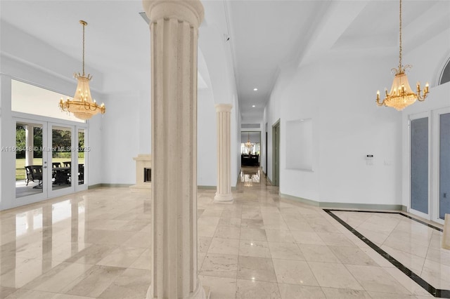 interior space with ornate columns, a high ceiling, a notable chandelier, and baseboards