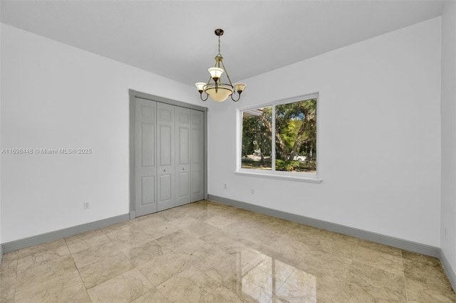 spare room featuring marble finish floor, baseboards, and a chandelier