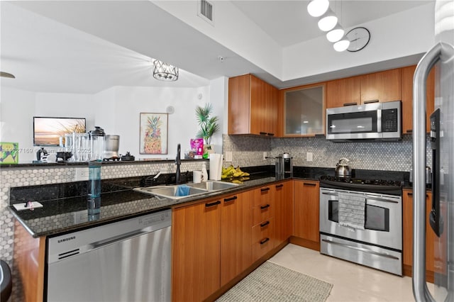 kitchen featuring appliances with stainless steel finishes, light tile patterned floors, decorative backsplash, sink, and dark stone counters