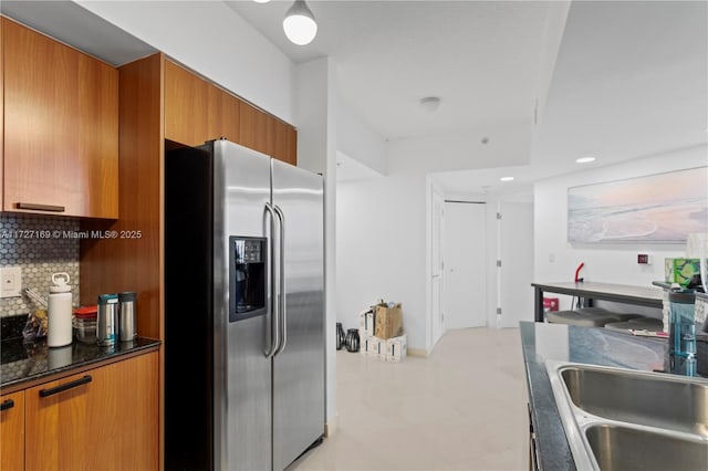 kitchen featuring sink, stainless steel refrigerator with ice dispenser, decorative backsplash, and dark stone countertops