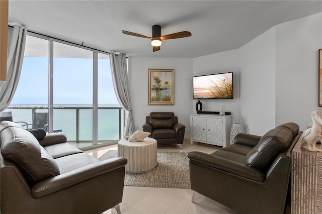 living room with ceiling fan, a water view, light tile patterned floors, floor to ceiling windows, and a textured ceiling