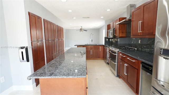 kitchen with wall chimney range hood, sink, dark stone countertops, stainless steel appliances, and kitchen peninsula