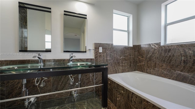 bathroom with tile walls, vanity, and tiled bath