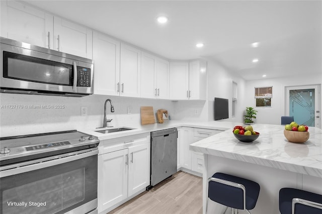 kitchen featuring white cabinetry, kitchen peninsula, appliances with stainless steel finishes, light wood-type flooring, and sink