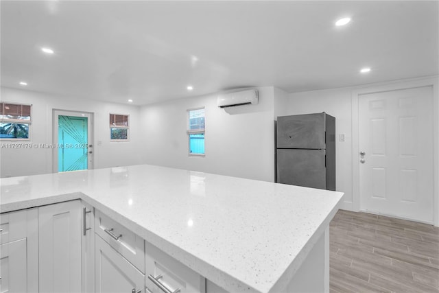 kitchen with light stone countertops, white cabinets, stainless steel fridge, and a wall unit AC