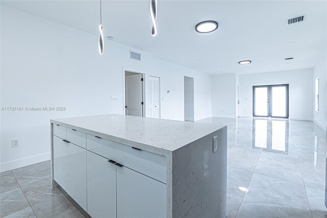 kitchen with white cabinets, french doors, light stone counters, and a kitchen island