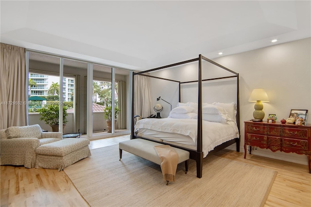 bedroom featuring access to exterior, hardwood / wood-style floors, and a tray ceiling