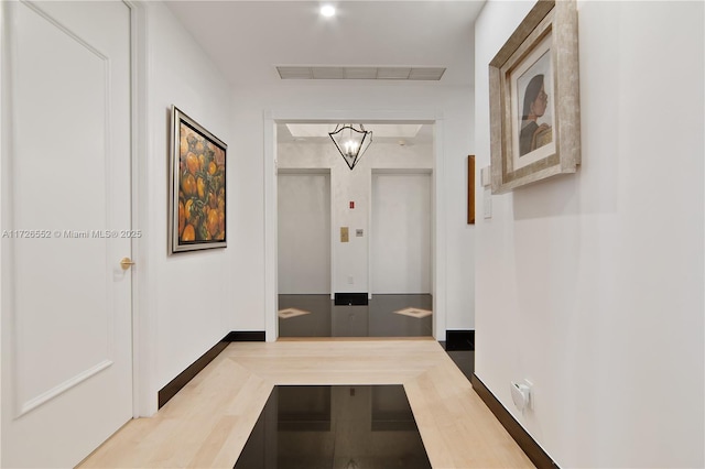 hallway featuring hardwood / wood-style flooring, elevator, and an inviting chandelier