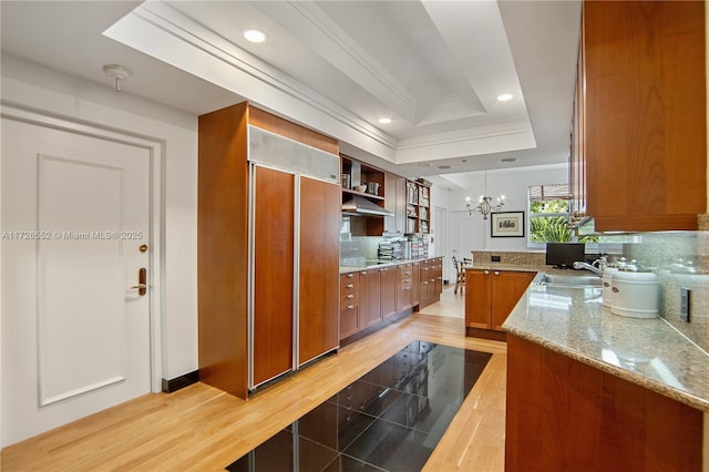 kitchen with decorative light fixtures, an inviting chandelier, paneled built in refrigerator, kitchen peninsula, and a tray ceiling