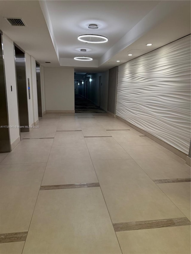 corridor featuring a raised ceiling, visible vents, elevator, light tile patterned flooring, and baseboards