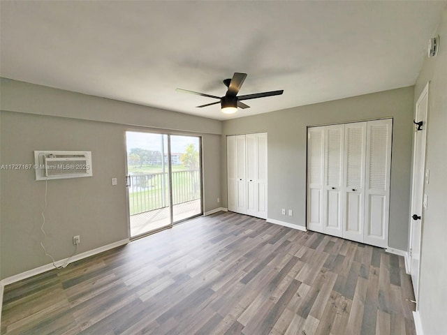 unfurnished bedroom with baseboards, a wall unit AC, wood finished floors, access to outside, and multiple closets