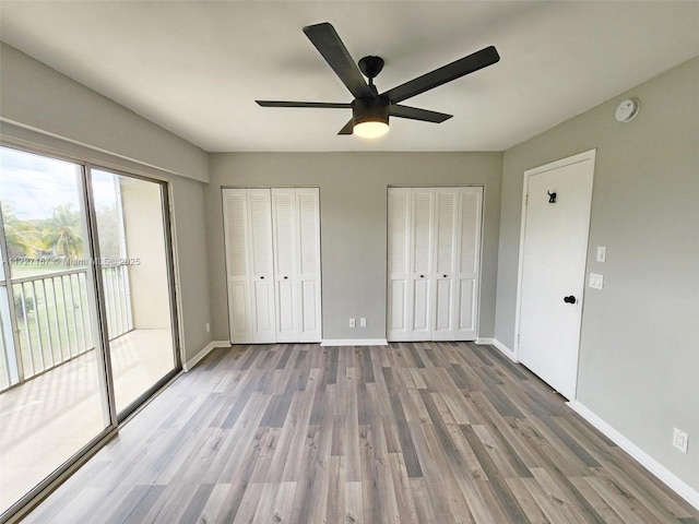 unfurnished bedroom featuring multiple closets, access to outside, baseboards, and wood finished floors