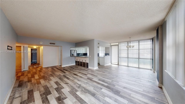 unfurnished living room featuring a textured ceiling, a wall of windows, light wood-type flooring, and a notable chandelier