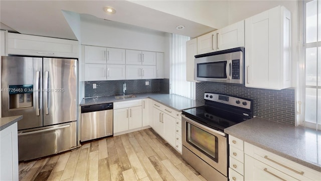 kitchen featuring white cabinets, appliances with stainless steel finishes, sink, backsplash, and light wood-type flooring