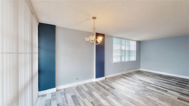 empty room with wood-type flooring, a textured ceiling, and a chandelier