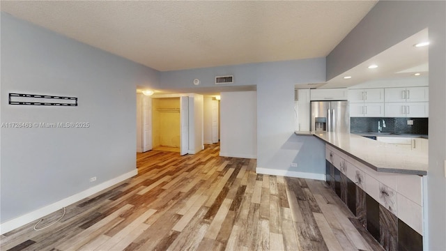 kitchen featuring a textured ceiling, white cabinetry, light hardwood / wood-style floors, backsplash, and stainless steel fridge